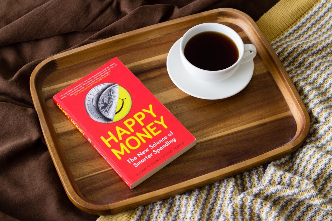 The book "Happy Money" and a cup of coffee on a wooden tray