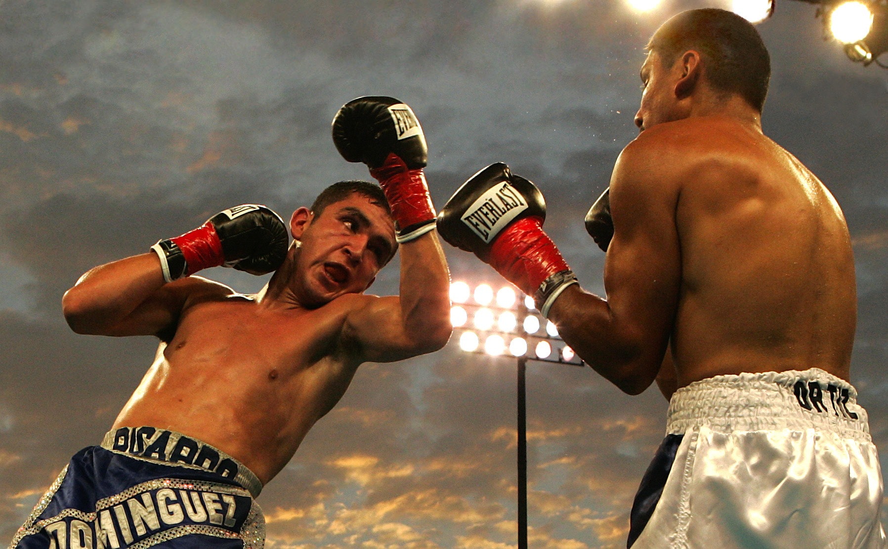 Two boxers, slick with sweat, face off under bright lights