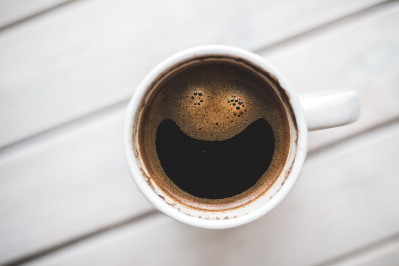 A cup of coffee from above. The foam on the top has the appearance of a pair of eyes and a wide smile.