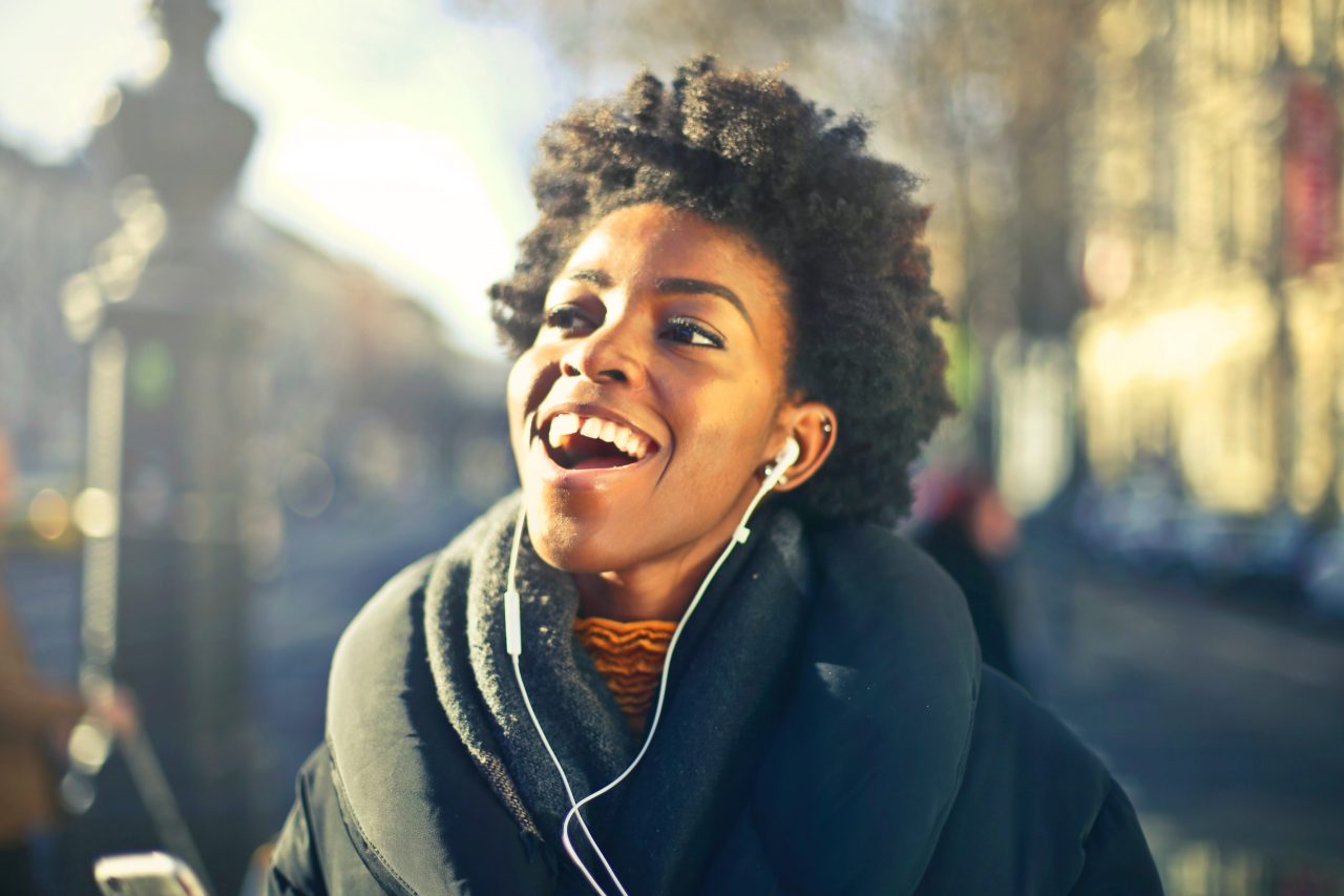 A brown-skinned woman wearing headphones and smiling widely