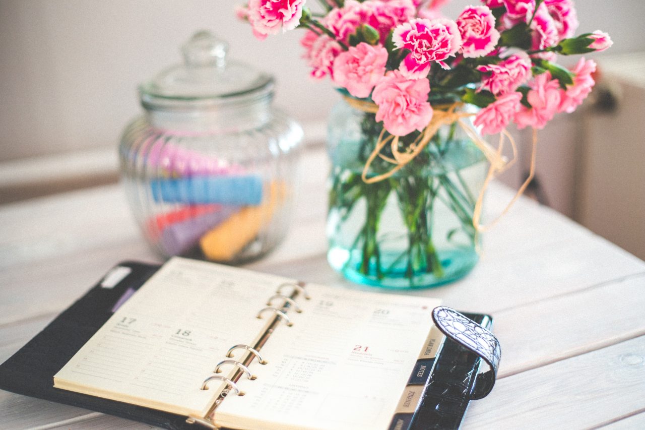 An open planner beside a bouquet of pink flowers