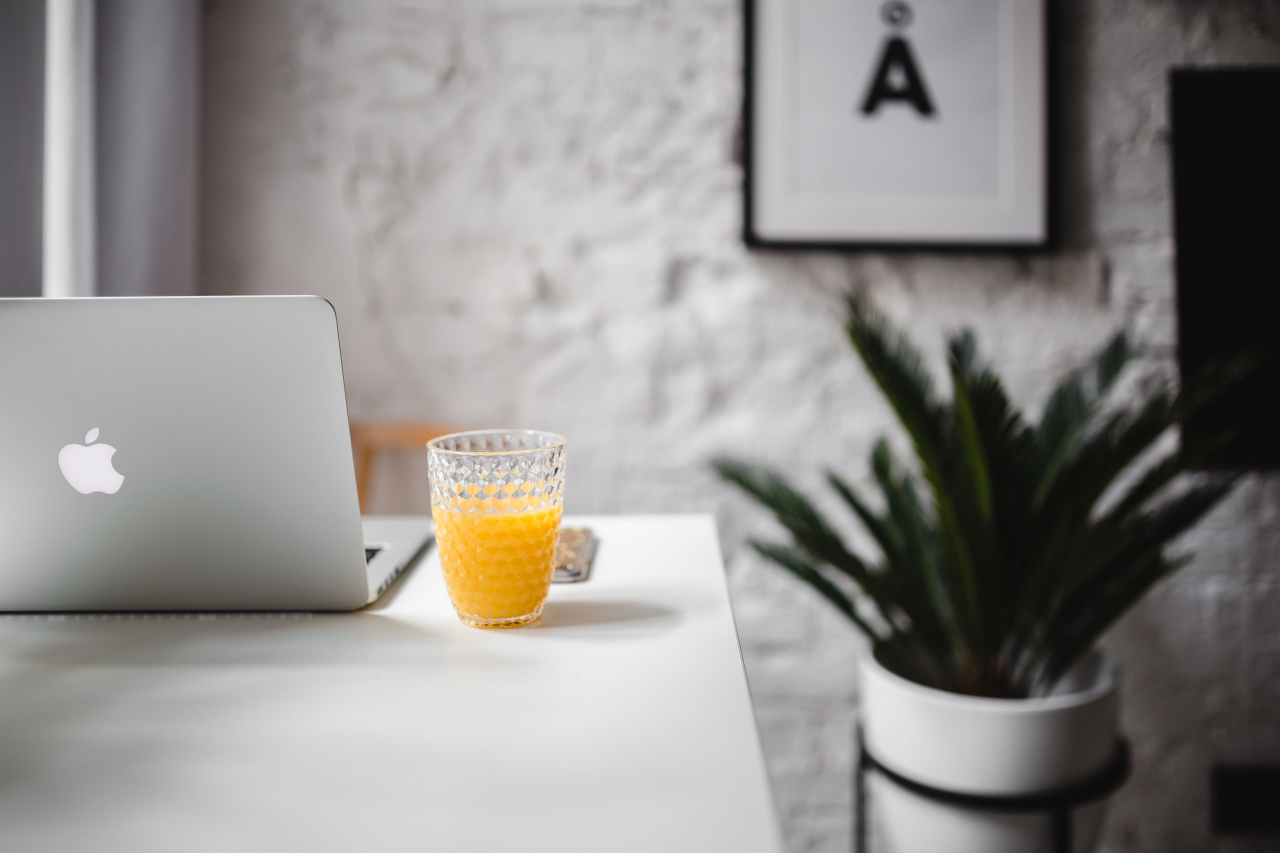 A laptop and a glass of orange juice on a white desk