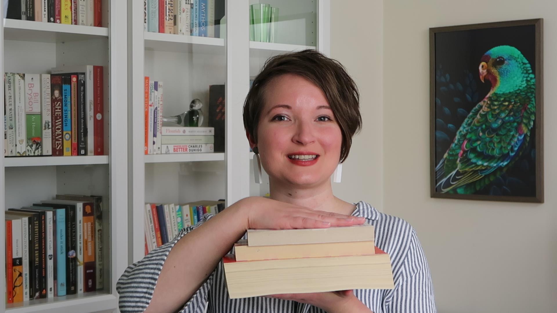Christina smiles, while holding up three books
