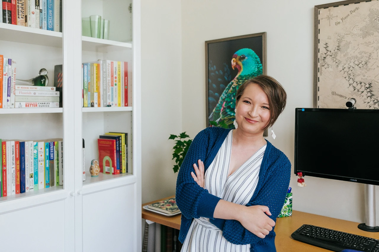 Christina Majoinen of Project TGL is standing in her office, wearing a blue crocheted cardigan. She has her arms folded confidently and is smiling warmly.