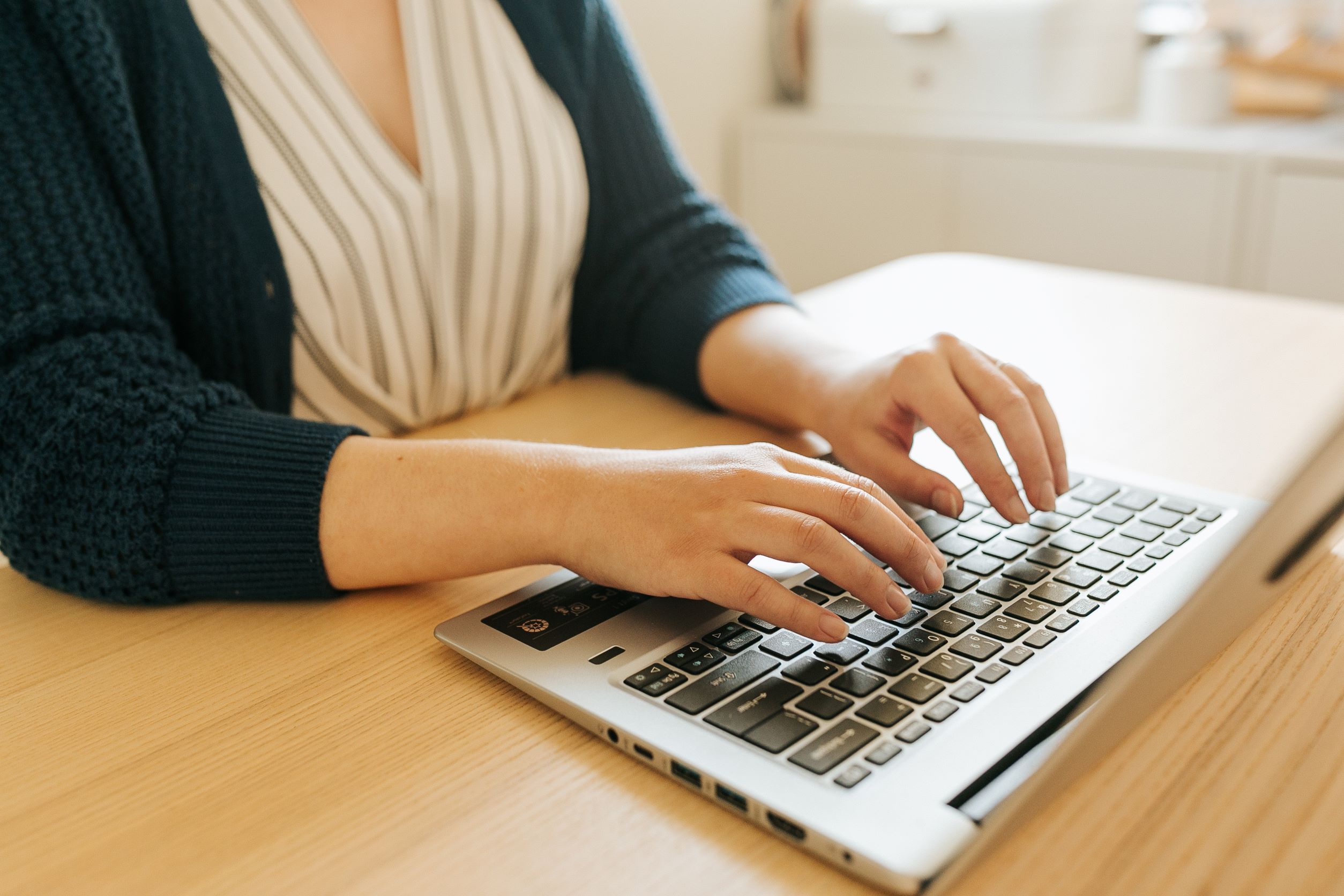 A fair-skinned woman's hands (Christina's hands) typing at a laptop keyboard