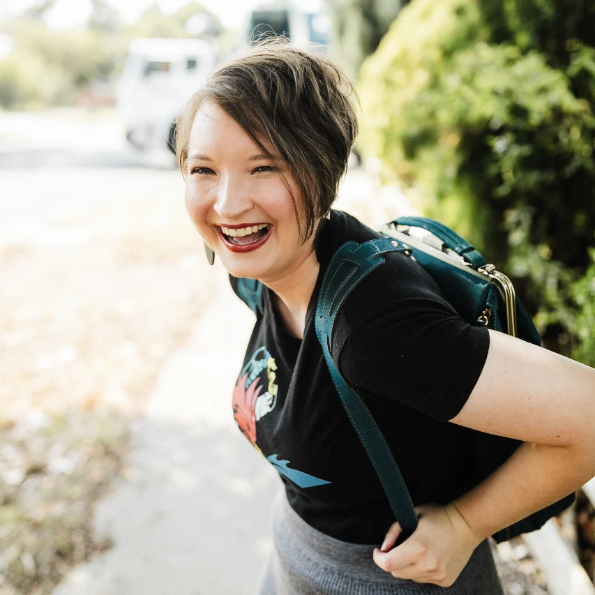 Christina is outdoors, laughing joyously, wearing a teal-coloured cork leather backpack.