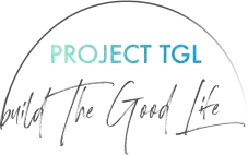 The Project TGL logo: The words "PROJECT TGL" appear in blue and green watercolour, with a sweeping grey half-circle drawn above them. Below are the words "build The Good Life" in a handwritten font.