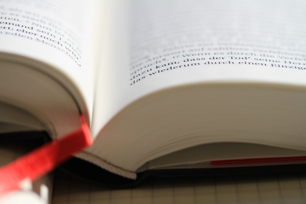A close-up for an open book with a red ribbon bookmark.